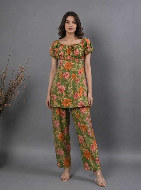 A woman modeling a two-piece floral print kurta and trouser set in olive green, with orange and pink flowers, against a solid gray studio background.