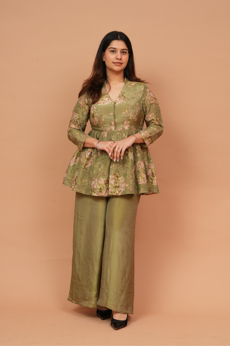 Woman wearing a green floral top and pants against a beige background