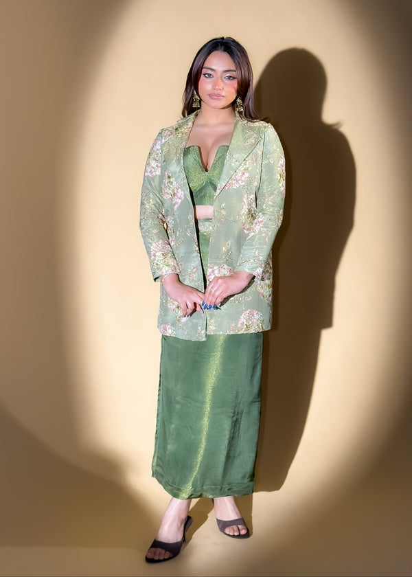 Woman in a green floral outfit standing against a beige wall with a spotlight effect.