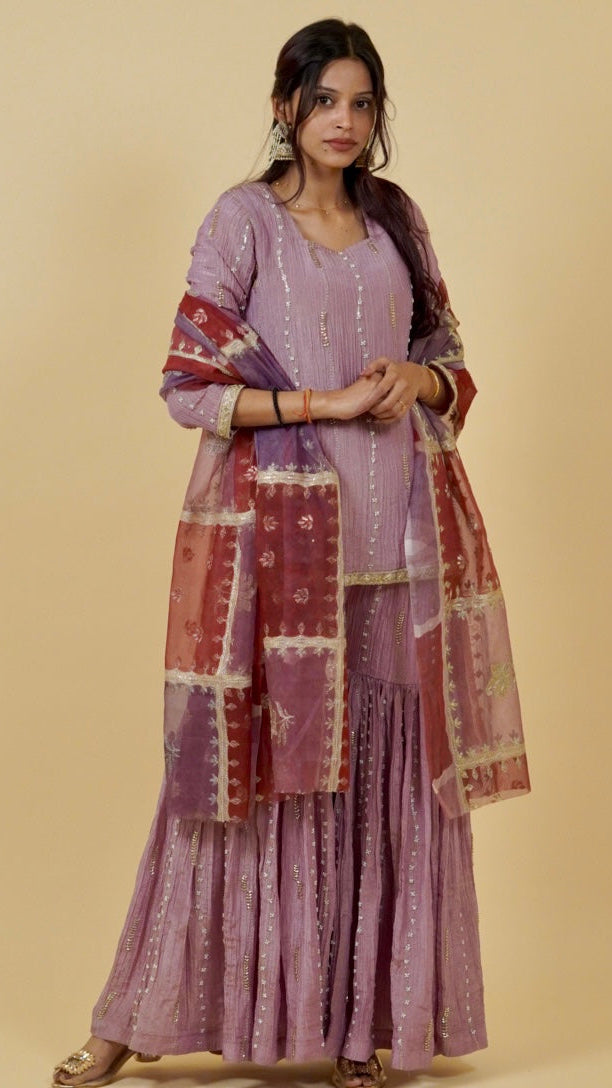 Woman wearing a traditional outfit with a purple dress and red dupatta on a beige background