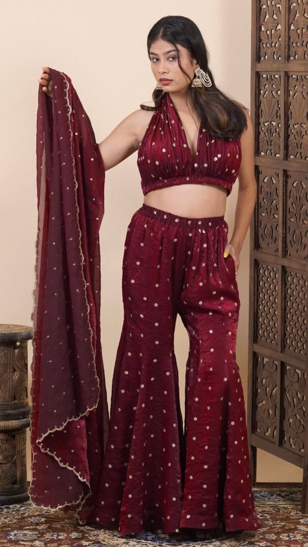 Woman in a maroon traditional outfit with a wooden carved screen in the background