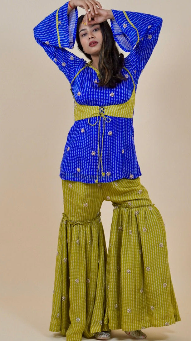 Woman wearing a blue top and green pants against a beige background