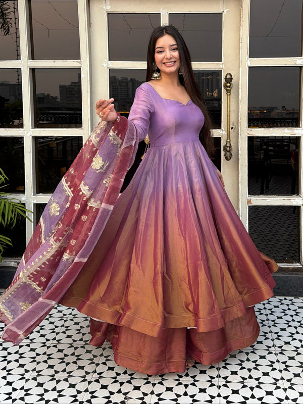Woman in a long, flowing dress standing in front of a decorative window.