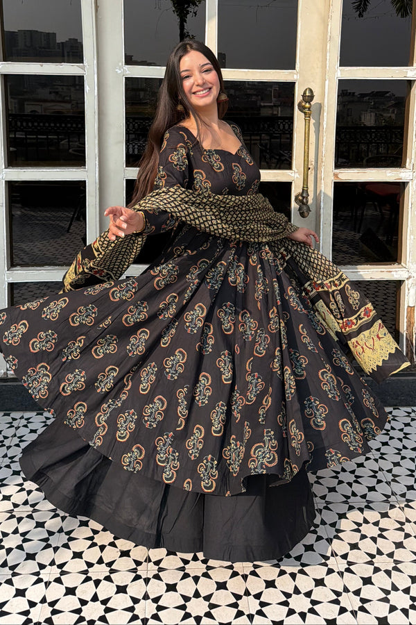 Woman in a traditional outfit standing in front of a hexagonal window with a geometric patterned wall.